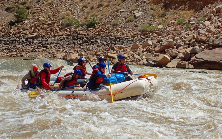 A group of students paddle a raft through whitewater.